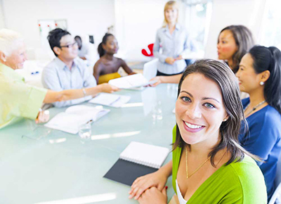 Woman smiles at a camera as a committee works to maximize special events behind her as part of fundraising for nonprofits.