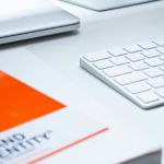 Brand identify book sitting on a white desk next to a white keyboard